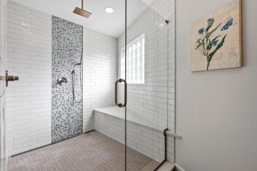 Large, walk-in shower with full subway tile surround w/ glass mosaic accents, rain and hand shower heads, bench and frameless glass door