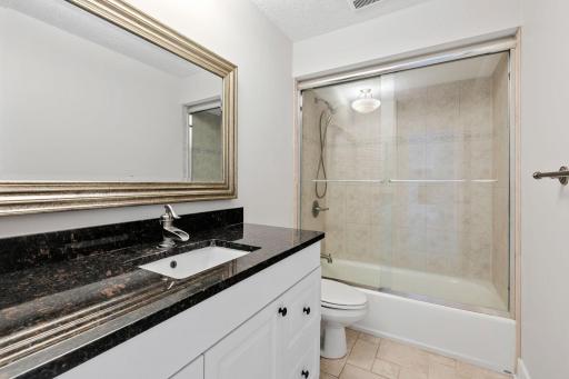 Full Bathroom offers enameled vanity cabinet w/ granite countertop, glass shower doors and tile tub surround and flooring