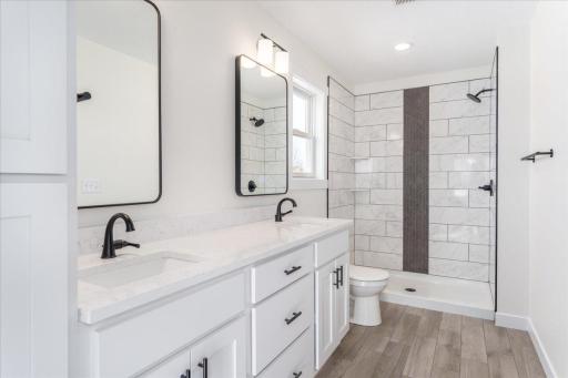 Primary bathroom ensuite with tile shower, two sinks, quartz counter top, and tile flooring.