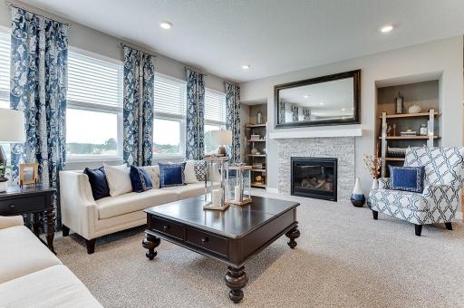 The family room is punctuated by a gas fireplace - which serves as a cozy bookend to the area and highlights a space that's flooded in natural light via these four soaring windows! *Photo of model home - colors and options may vary*