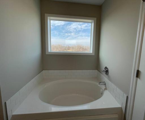 Deluxe Primary Bath Soaking Tub features a tile surround and window with backyard nature views.
