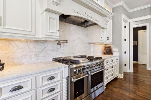 Decorative toe kick on cabinets, marble countertops & backsplash, pot filler above THOR 48-inch 6 burner gas range. Stunning wood hood.