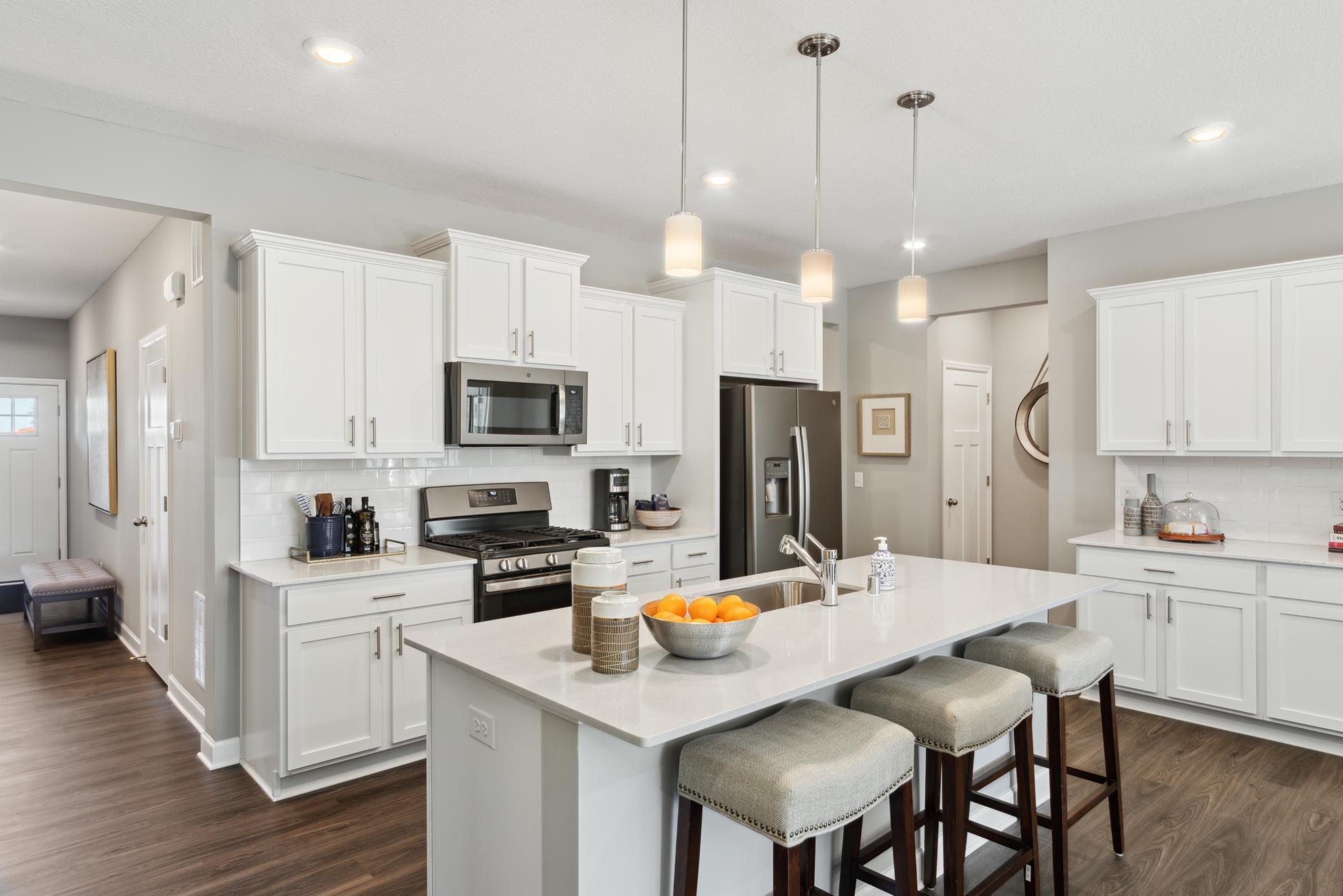 (Photo of completed model home, actual home's finishes vary) This large kitchen features stainless steel appliances and a spacious quartz center island. Notice the abundance of cabinet and counter space!