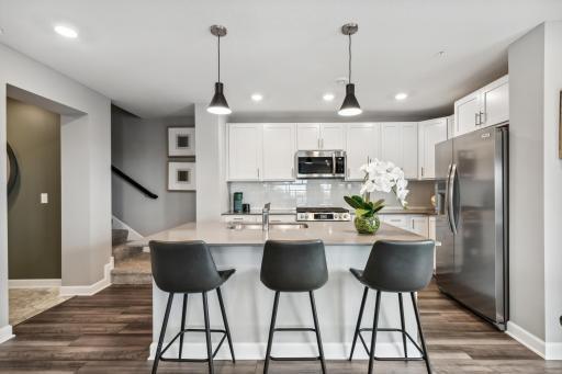 (Photo of decorated model, actual home's finishes vary) This spacious kitchen features a large center island with quartz countertops, under mount sink, recessed lighting, LVP hardwood floors, stainless appliances and more!