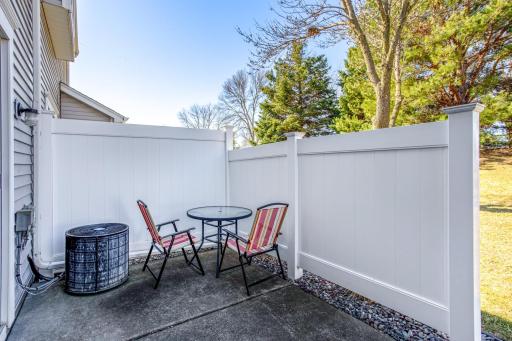 Private patio with vinyl fencing adjacent to open green space surrounded by mature trees and convenient access to walking paths.