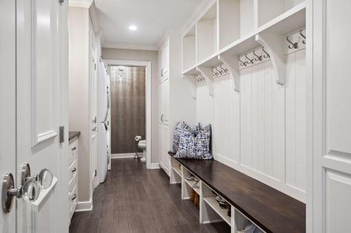 The mudroom is a functional yet stylish space, featuring a drop desk, chrome fixtures, and glass knobs. Lockers, a bench, and closets provide ample storage, while the adjacent laundry area offers stackable washer/dryer, and a powder room.