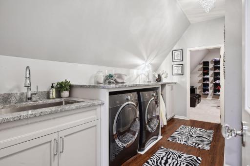 Through the door lies the second floor laundry, featuring two chandeliers, large stainless steel sink, hanging rack for clothing, and ample storage.