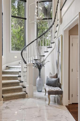 A winding staircase graced by a chrome chandelier ascends to the upper level, offering a stunning focal point.