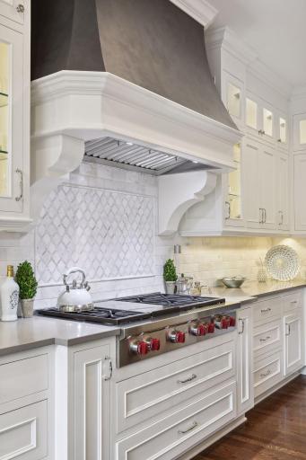 Pendant lights illuminate the space, which features a gas Wolf cooktop, a striking tile backsplash, and decorative range hood.