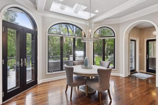 The informal dining area, illuminated by a chandelier and framed by large arched windows. A doorway provides access to the deck, blurring the lines between indoor and outdoor living.