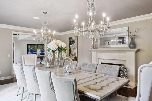 Crown molding adorns the ceiling, while a gas fireplace adds a touch of warmth and intimacy. Two chandeliers cast a warm glow, and the ceiling is detailed with elegant wallpaper, further enhancing the room's charm.