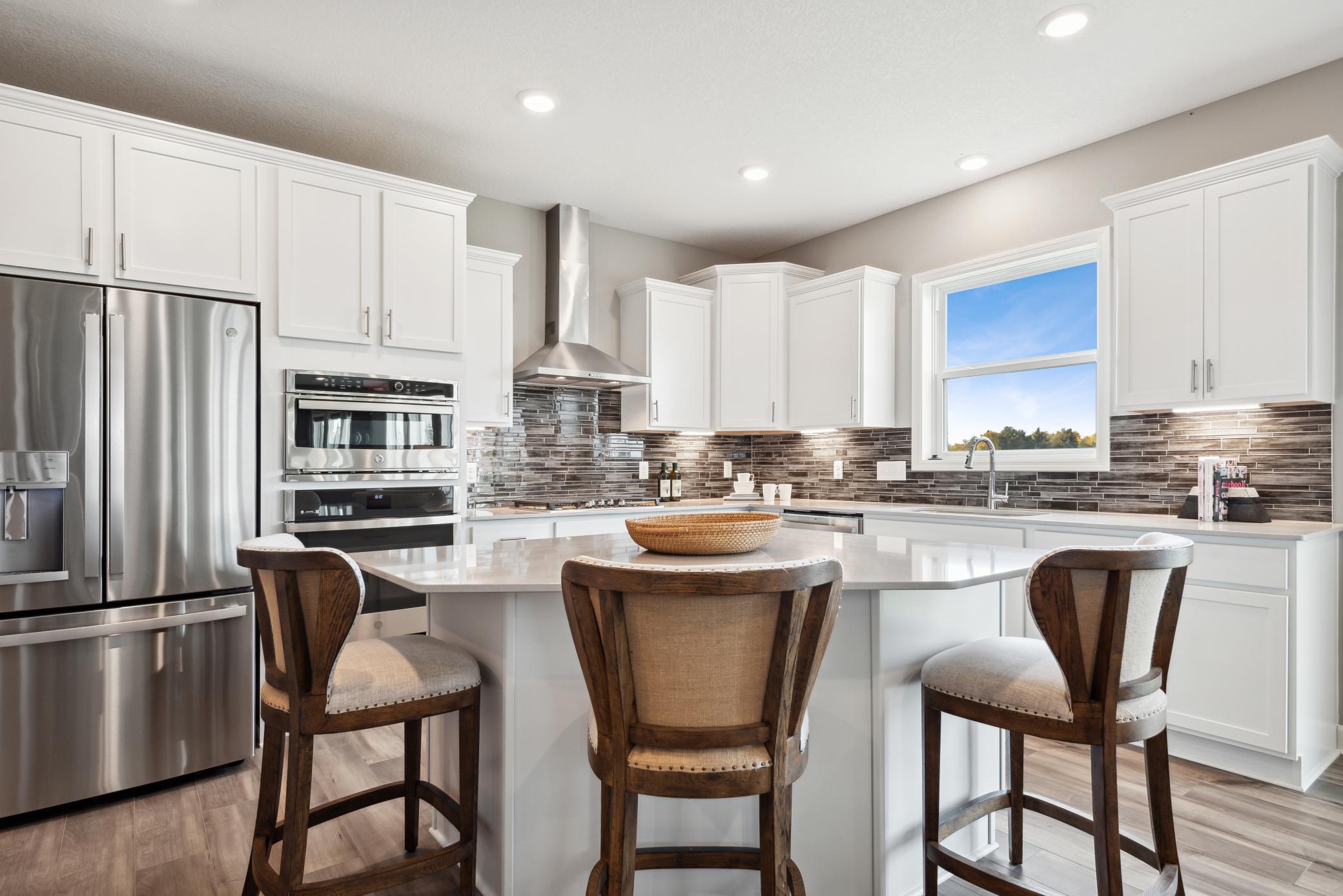 (Photo of a decorated model, actual homes finishes will vary) Large gourmet kitchen anchored by a large kitchen island. Features stainless steel appliances, quartz counters, a walk-in pantry, LVP floors, double ovens and more!