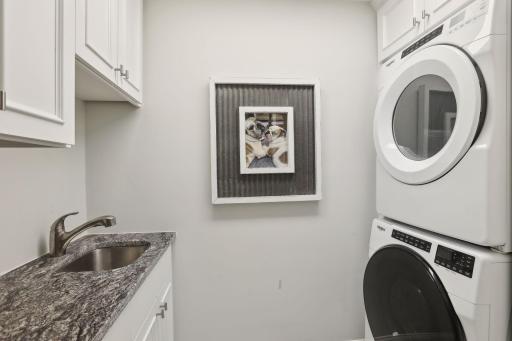 Upper level laundry with sink, cabinetry and full sized stacked appliances