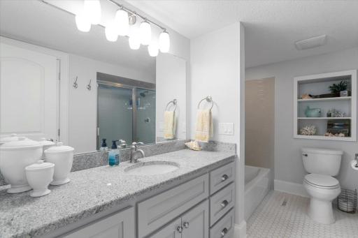 Beautiful 2nd primary bathroom with built in shelving, granite countertops, and full shower with separate bathtub.