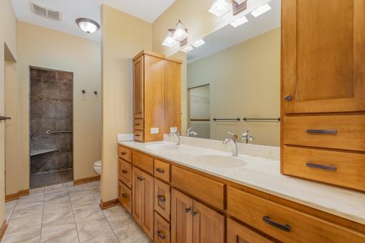 The primary bathroom features: a 9 foot knock down ceiling; a walk-in shower w/seat bench & product cubby; custom, maple cabinets; solid surface countertop w/double sinks; under cabinet floor lighting w/motion sensor, and heated tile floor.
