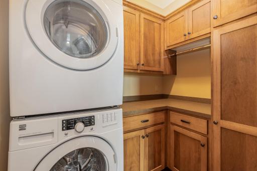 The main floor laundry room features: a 9 foot knock down ceiling, stackable Kenmore washer & dryer; custom, built in cabinets & broom closet; a folding counter & hanging bar; and luxury vinyl tile flooring.