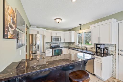 Updated kitchen with white cabinetry, granite counters, tiled flooring & backsplash, SS appliances and hardware.