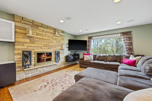 Expansive living room with large window, woodburning fireplace, recessed lighting, in-ceiling speakers, laminate flooring, and white trim. (fire in photo is virtually staged)