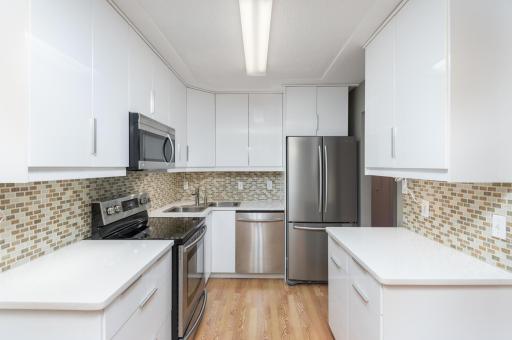 Updated, clean white cabinetry with soft close doors, Corian counter tops, tile back splash and stainless appliances.