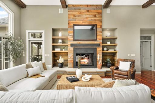 Built-in shelving, hidden TV picture frame, and functional fireplace and reclaimed wood beams across living and foyer.