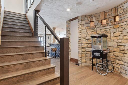 Descend the lower level staircase, flanked by stone wall where rustic charm meets architectural sophistication, creating a dramatic entrance to the inviting lower level.