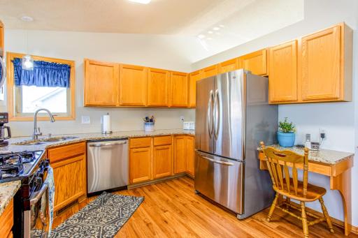 Vaulted kitchen with granite countertops, laminate wood flooring, stainless-steel appliances, and a corner sink.