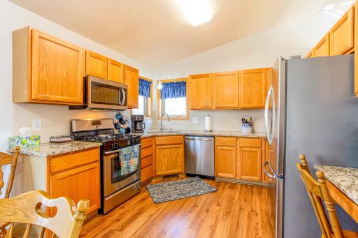 Vaulted kitchen with granite countertops, laminate wood flooring, stainless-steel appliances, and a corner sink.