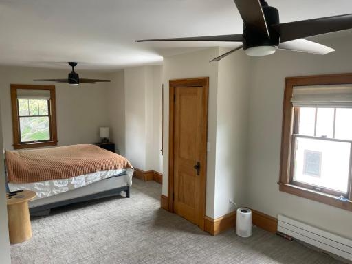 Spacious primary bedroom with new carpeting and two closets and ceiling fans.