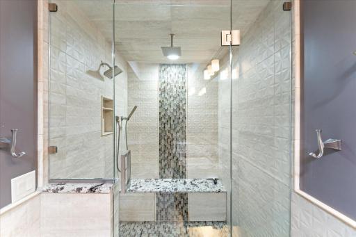 Walk-in shower with beautiful tile work, bench and multi-head shower heads.