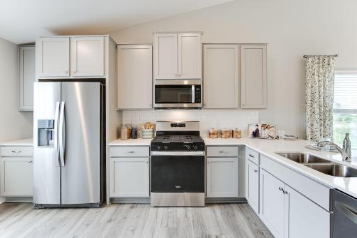 Kitchen shown with white cabinets, gas oven/range, microwave over cooktop, and quartz countertops. Photos is of model home. Colors and options may vary. Ask Sales Agent for details.