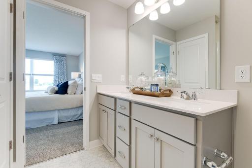 A peak inside the bathroom off the Primary Suite. Notice the extra high cabinets and double-bowl Quartz covered vanity with loads of storage! Photo is of model home. Colors and options may vary. Ask Sales Agent for details.