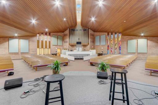 Sanctuary accented with stained glass windows, skylights, and wood paneled ceiling.