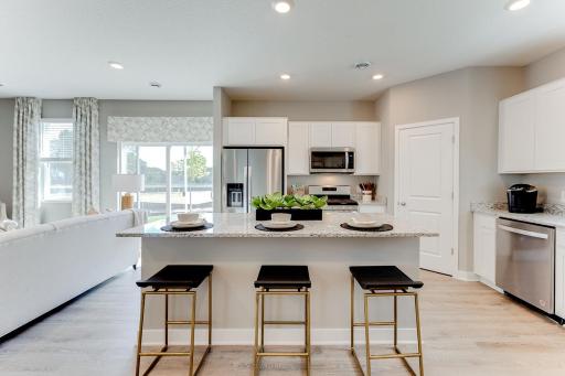 The kitchen is home to a large center island complete with quartz countertops, stainless appliances, including a luxurious gas range. Model home photo, actual home will vary in finishes.