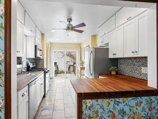 Bright and sunny open kitchen with white cabinetry and stainless appliances.