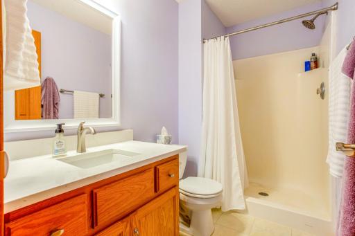 This charming master bathroom features soft lavender walls paired with a crisp white shower and vanity, offering a refreshing space to start your day. The large mirror and tasteful accents ensure both style and functionality.