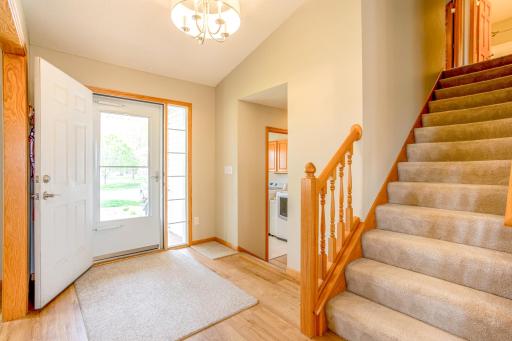Welcome home through this bright and inviting entrance hall, showcasing a beautiful staircase with wooden accents that lead to the kitchen and dining room. The well-lit space features luxury vinyl wood flooring, perfect for bustling family life.