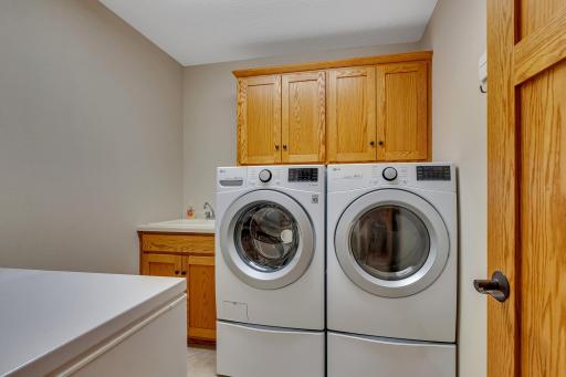 Main level laundry room with ceramic tile flooring, utility sink, cabinets above the washer and dryer and the washer and dryer are LG front load with storage cabinets below each unit!