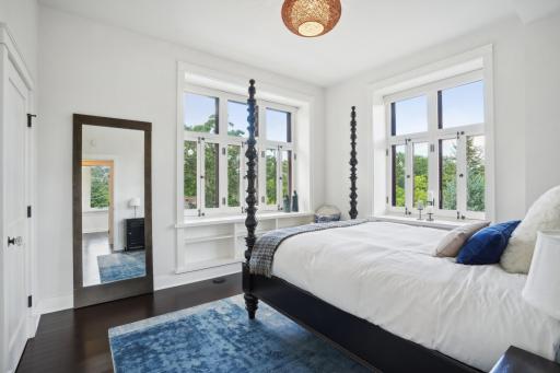 Originally the primary suite, bedroom two on the main floor features generous custom book cases, lots of custom storage solutions in its dual closets, and more panoramic treetop views