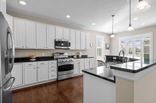 The open main level invites you into a kitchen that boasts stainless steel appliances, pendant lighting, and pristine white cabinetry.