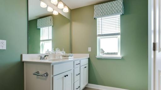 A peak inside the bathroom off the Primary Suite. Notice the extra high cabinets and double-bowl Quartz covered vanity with loads of storage! Photo is of model home. Colors and options may vary. Ask Sales Agent for details.