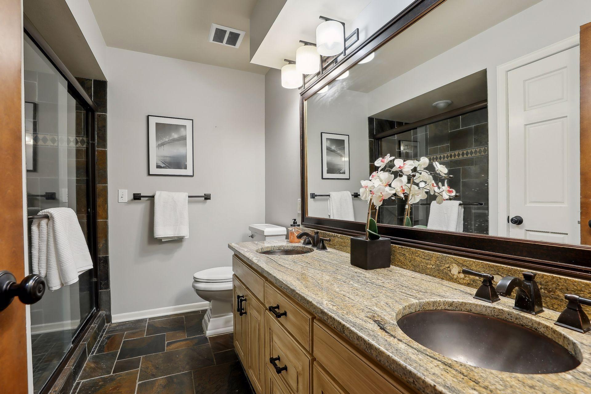 Stylish main level bathroom w/ slate tiled floors and shower, double sinks and beautiful white accent trim.