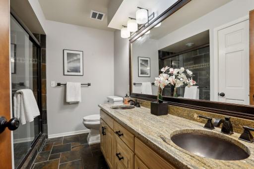 Stylish main level bathroom w/ slate tiled floors and shower, double sinks and beautiful white accent trim.