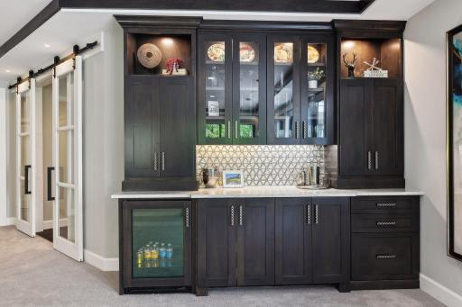 The walk-up bar has been crafted from clear alder and offers cabinetry with pull-out shelving, a liquor drawer, quartz countertop and a beverage refrigerator.