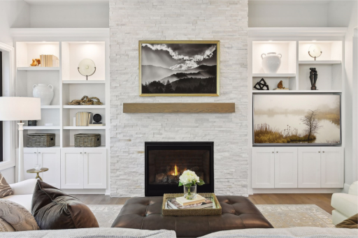The gas fireplace features a floor-to-ceiling chase of cut stone tile and is flanked by built-in bookcases and cabinetry featuring soft-close doors and accent lighting.
