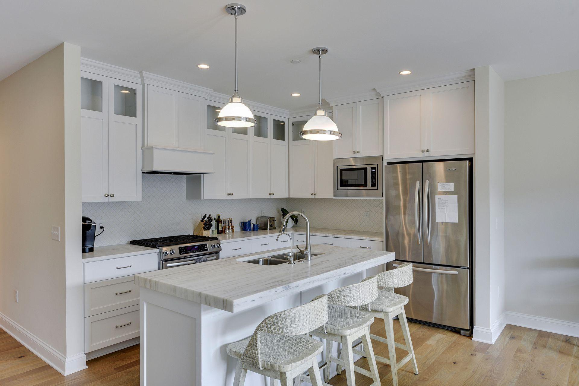 Kitchen features SS appliances, gas range, crisp white tiles and cabinetry