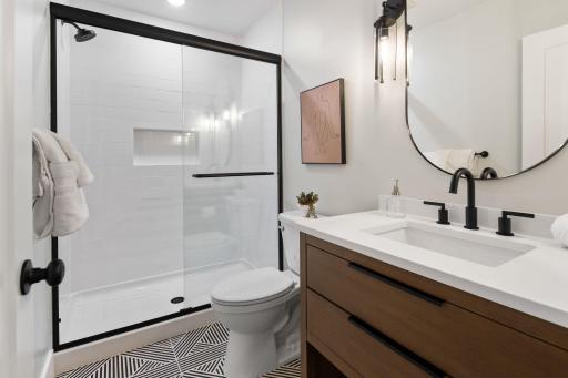 Lower level bath with black metal accents, warm wood tones and graphic tile floor