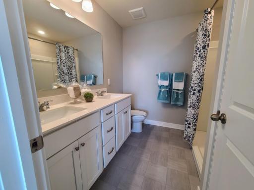 A peak inside the bathroom off the Primary Suite. Notice the extra high cabinets and double-bowl Quartz covered vanity with loads of storage! Photo is of actual home. Colors and options may vary. Ask Sales Agent for details.