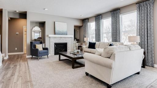 The family room is punctuated by a gas fireplace - which serves as a cozy bookend to the area and highlights a space that's flooded in natural light via these three soaring windows overlooking the back of the home! (Photo of model, colors may vary)
