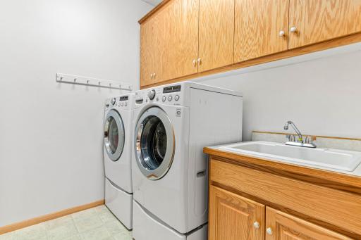 Main floor laundry room features front loading washer and dryer units atop a sturdy base. Adjacent, a utility sink nestled within cabinetry offers convenience in a modern efficient space.