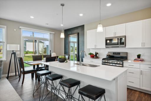 Spacious kitchen with large island, quartz countertops, tile backsplash, white cabinets, pull out trash/recycling cabinet and the popular slate finish appliances! *Photos of model home; colors and finishes will vary.